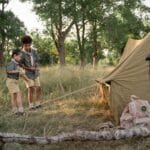 Dwoje dzieci rozbija namiot w lesie podczas wspólnego biwaku