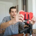 Mężczyzna w domu ustawia smartfon na statywie do nagrywania vloga