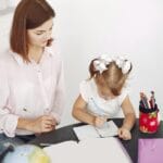 Dziewczynka rysuje w notesie przy okrągłym stole obok siedzącej mamy