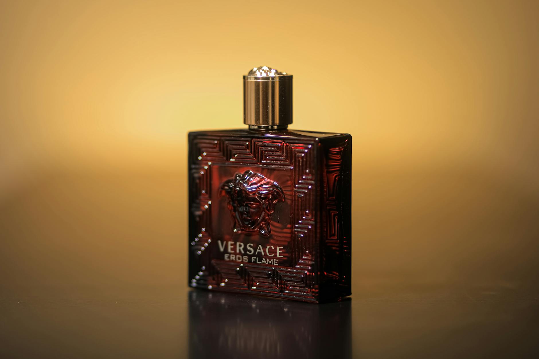 Flakon perfum Versace Eros Flame na tle ciepłego żółtego koloru
