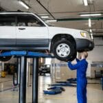 Mechanik ogląda białego SUV-a na podnośniku w jasnym warsztacie samochodowym